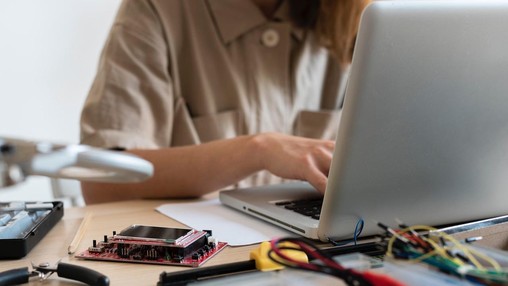 Jeune femme travaillant sur un ordinateur et entourée de composants électroniques Jeune femme travaillant sur un ordinateur et entourée de composants électroniques